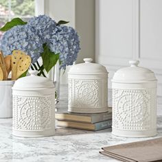 three white canisters sitting on top of a counter next to a vase with blue flowers