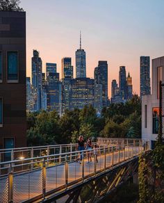 people walking across a bridge over a river in front of the city skyline at sunset