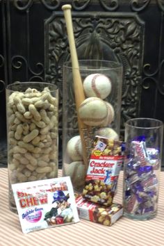 a table topped with glasses filled with candy and baseballs next to a wooden bat