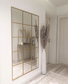 a tall white vase sitting next to a mirror on top of a wooden floor in front of a door