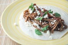 a tortilla topped with shredded meat, cheese and cilantro sauce on a yellow plate