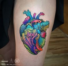 a colorful heart tattoo on the thigh with fish and waves coming out of it's center