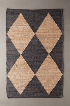 an area rug with black, tan and white squares on it's sides is shown in front of a gray wall