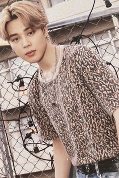 the young man is posing in front of a chain link fence with his hand on his hip