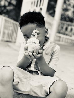 a young boy sitting on the ground holding a cupcake in front of his face