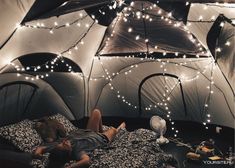 a person laying on a bed in a tent with lights strung from the ceiling above it