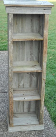 a wooden book shelf sitting on the side of a sidewalk next to a grass field