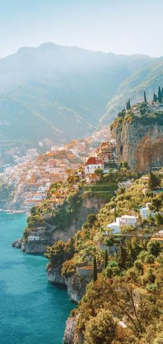 an aerial view of a town on the edge of a cliff overlooking water and mountains