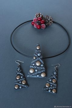 three pieces of jewelry sitting on top of a table next to berries and pine cones