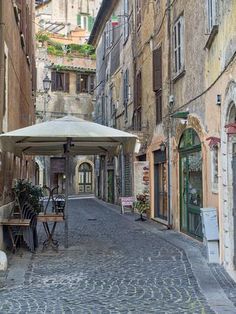 an alleyway with tables and umbrellas in the middle of it, surrounded by old buildings