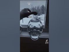 a hand is holding a glass bottle in front of a window with snow outside it