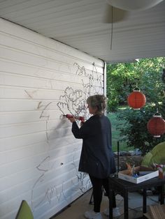 a woman writing on the side of a white wall with paper lanterns hanging from it