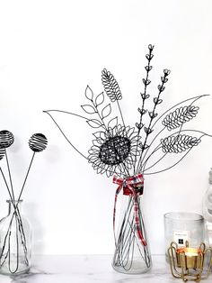 three glass vases with plants in them on a table next to candles and other items