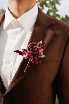 a man in a brown suit with a red boutonniere on his lapel