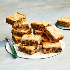 a white plate topped with lots of brownies and pieces of cake next to a knife