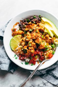 a white bowl filled with rice, meat and veggies next to an avocado