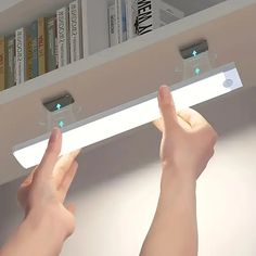 two hands are holding the remote control for a ceiling fan in front of bookshelves