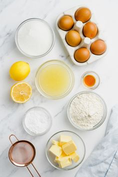 ingredients to make lemon cake laid out on a marble counter top, including eggs, butter, flour, and sugar