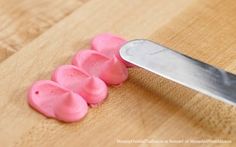 a knife is cutting up pink candy on a wooden surface with three pieces cut in half