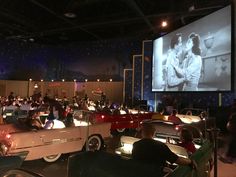 people sitting in cars watching a movie on a large screen at the back of a theater