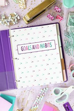 a binder with the words goals and habit bits on it surrounded by office supplies