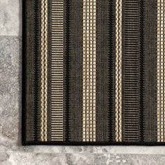 a black and beige rug with stripes on the floor in front of a stone wall