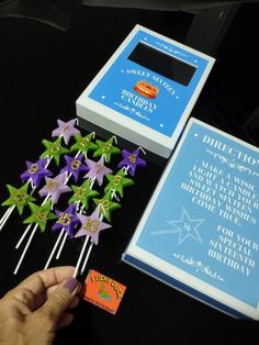 a hand is holding some purple and green pinwheels next to a blue box