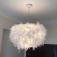 a chandelier made out of feathers hanging from the ceiling in a room with white walls