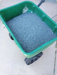 a green wheelbarrow filled with gravel on top of a cement floor next to a sidewalk