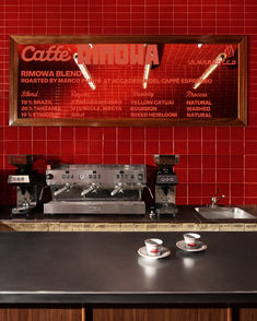 there is a coffee shop with red tiles on the wall and black countertops, along with two espresso machines