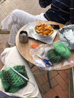 a table topped with yarn and other items on top of a wooden table next to a person