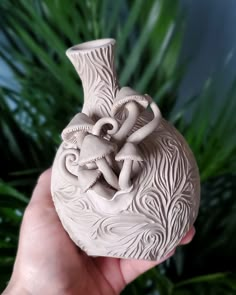 a hand holding a ceramic vase with two elephants on it's face and leaves in the background