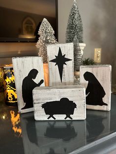 three wooden nativity blocks sitting on top of a table next to christmas trees and decorations