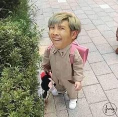 a young boy is standing next to a bush with a stuffed animal in it's lap