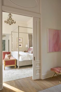 an open door leading to a bedroom with a white bed and pink chair in it