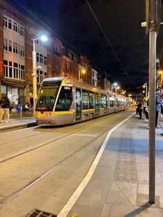 a yellow and white train traveling down tracks next to tall buildings on a city street