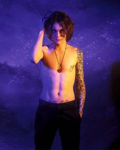 a shirtless man with tattoos on his chest and arm, standing in front of a purple background