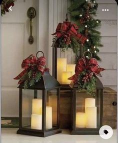 three lit candles with bows on them are sitting in front of a christmas wreath and door