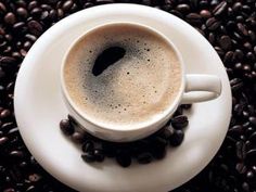 a cup of coffee sitting on top of a white saucer next to some beans