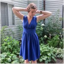 a woman in a blue dress is standing near some bushes and flowers with her hands on her head