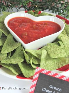 a heart shaped bowl filled with salsa on top of tortilla chips next to a sign