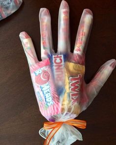 a hand made out of candy wrapper sitting on top of a wooden table next to an orange ribbon