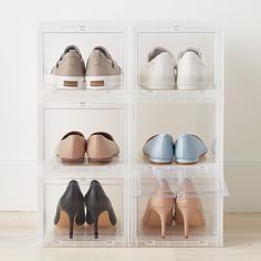 four clear bins filled with different types of women's shoes on top of a wooden floor