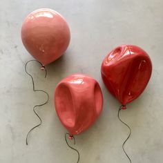 two red balloons sitting next to each other on a white surface with wires running through them