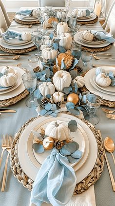 the table is set with blue and white dishes, silverware, and pumpkins