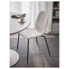 a white chair sitting next to a table on top of a carpeted floor in front of a window