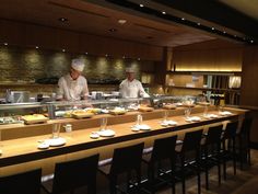 two chefs preparing food behind the counter in a restaurant or bar with lots of chairs