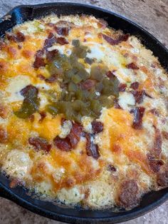 a pizza with cheese and toppings in a black pan on a stone counter top