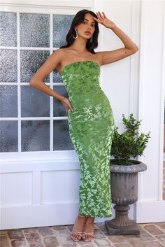 a woman in a green strapless dress leaning against a wall with her hand on her head