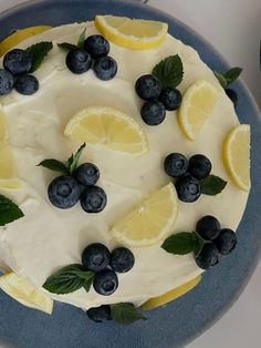 a cake with lemons, blueberries and mint leaves on it is sitting on a plate